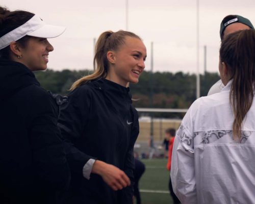 Emilie Girard et d'autres athlètes, discutant et rigolant après une séance d'entraînement sur une piste d'athlétisme.